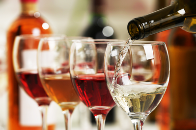 line of wine glasses being poured with bottles in the background